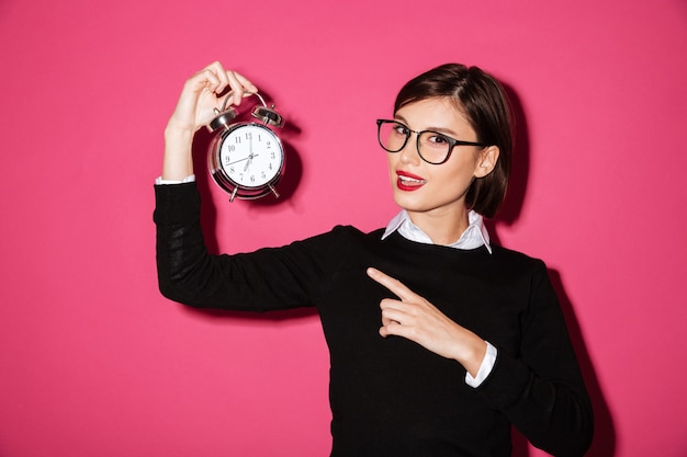 Portret szczęśliwy młody bizneswoman wskazuje przy zegarowym alarmem
