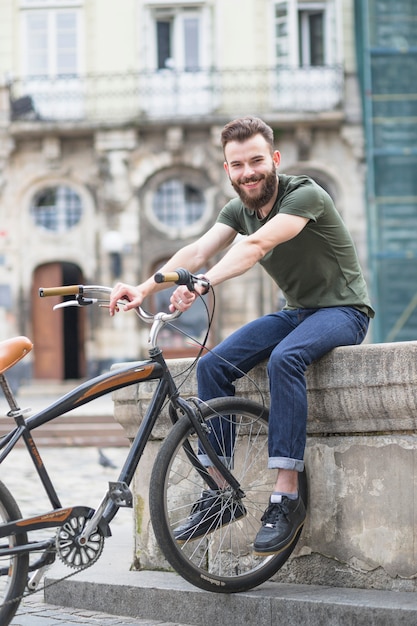 Bezpłatne zdjęcie portret szczęśliwy młody męski cyklista z bicyklem