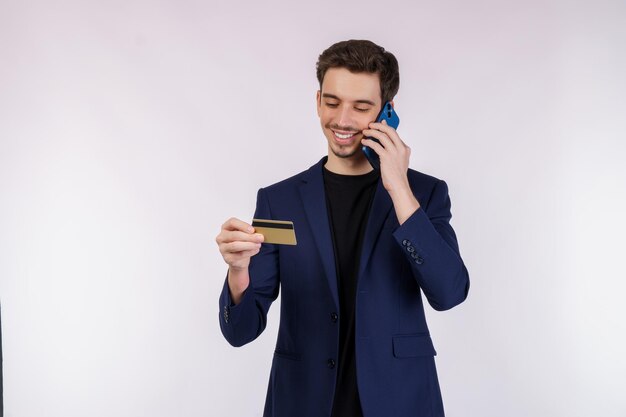 Portret szczęśliwy przystojny biznesmen opowiada telefonem komórkowym i trzyma kartę kredytową odizolowywającą nad białym tłem