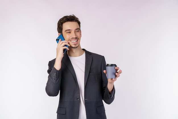 Portret szczęśliwy przystojny biznesmen rozmawia przez telefon komórkowy i trzyma gorącą kawę na białym tle nad białym tłem