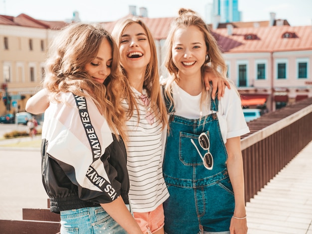 Bezpłatne zdjęcie portret trzech młodych pięknych uśmiechniętych hipster dziewcząt w modne letnie ubrania. seksowne beztroskie kobiety pozowanie na ulicy. pozytywne modele zabawy. przytulanie