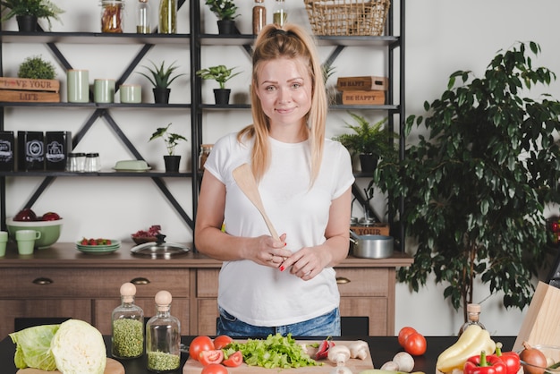 Bezpłatne zdjęcie portret trzyma drewnianej szpachelki pozycję w kuchni młoda kobieta