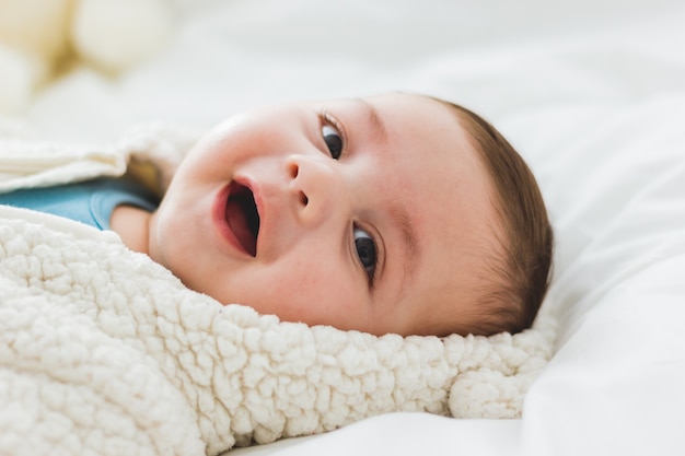 Portret uroczego 3-miesięcznego dziecka uśmiechniętego leżącego w łóżku z białych prześcieradeł