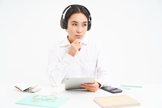 Portret uroczej biurowej kobiety w słuchawkach siedzi w miejscu pracy z cyfrowym tabletem słucha o