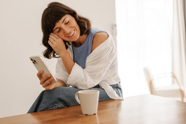 Portret uroczej kobiety z kawą uśmiecha się do telefonu