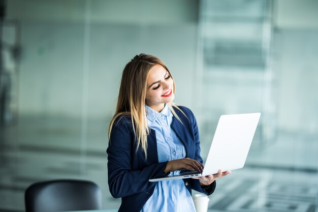 Portret uroczej, miłej, pozytywnej kobiety w okularach na głowie mając laptopa w rękach patrząc stojąc w miejscu pracy, stacja