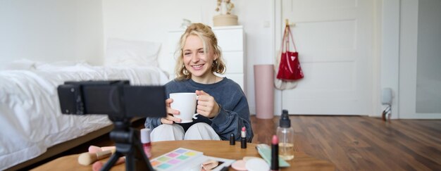 Portret uroczej uśmiechniętej kobiety, blondynki pijącej herbatę i nagrywającej wideo blog o zwykłym stylu życia