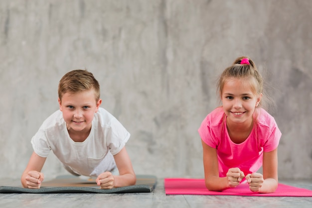 Portret uśmiechnięta chłopiec i dziewczyna robi sprawności fizycznej ćwiczeniu przed betonową ścianą