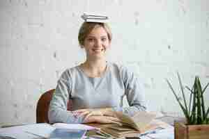 Bezpłatne zdjęcie portret uśmiechnięta kobieta na biurko, książek na głowie