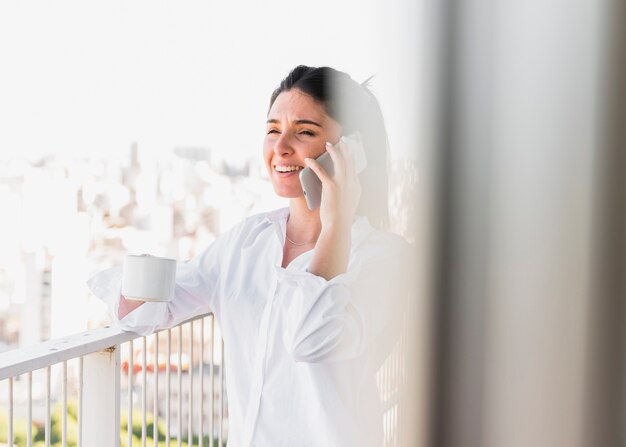 Portret uśmiechnięta kobieta trzyma filiżankę opowiada na telefonie komórkowym