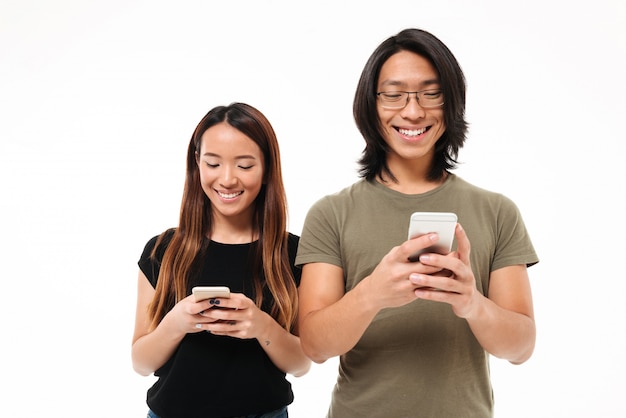 Portret uśmiechnięta młoda azjatykcia para używa telefony komórkowych