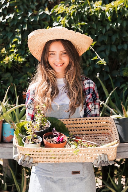 Portret uśmiechnięta młoda kobieta trzyma doniczkowe rośliny w koszu