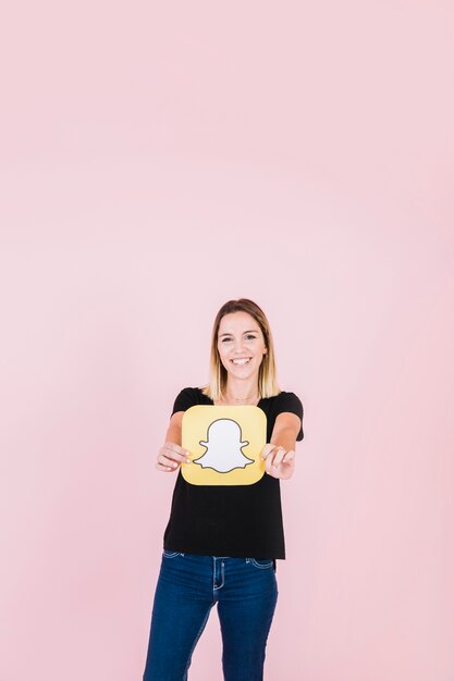Portret uśmiechnięta młoda kobieta trzyma snapchat ikonę