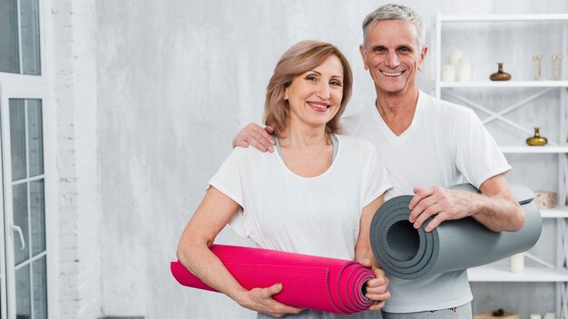 Portret uśmiechnięta para starszych w odzież sportowa przewożących maty do jogi