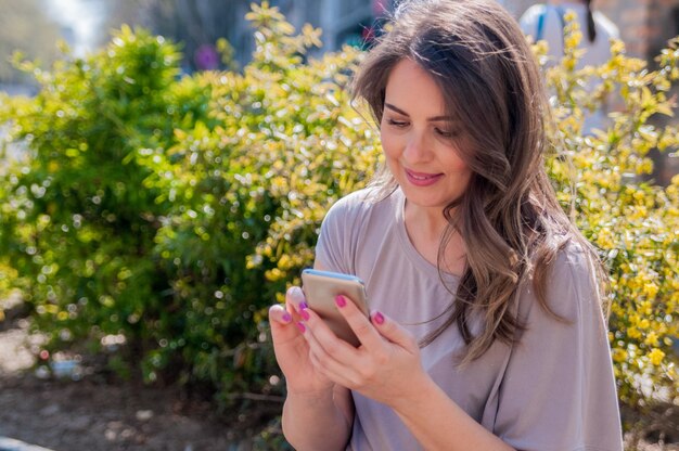 Portret uśmiechnięta piękna kobieta texting z jej telefonu. Atrakcyjna kobieta przy użyciu telefonu komórkowego na zewnątrz pomieszczeń.