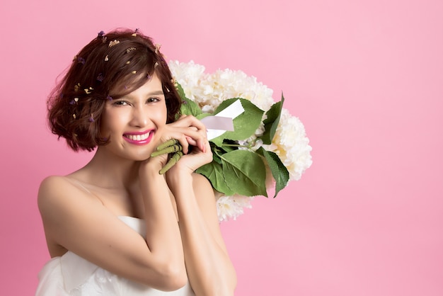 Portret uśmiechnięte figlarnie ślicznej kobiety mienia kwiaty odizolowywający na menchiach