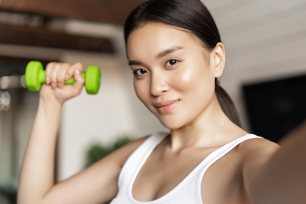 Portret Uśmiechniętego Azjatyckiego Instruktora Fitness Robi Selfie Z Hantlami Wysportowana Kobieta Robi Zdjęcie...