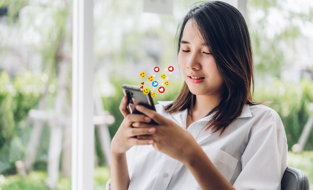 Portret uśmiechniętego szczęśliwego piękna azjatycka kobieta relaksuje korzystanie z technologii cyfrowej komunikacji społecznej ze smartfonem. młoda azjatycka dziewczyna patrzy na ekran telefonu komórkowego z ikoną mediów społecznościowych online w kawiarni