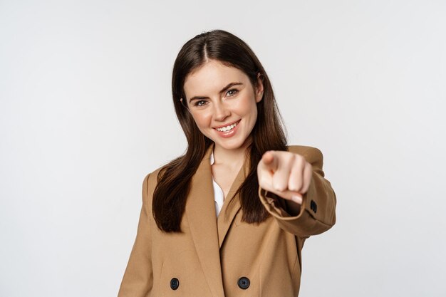 Portret uśmiechniętej entuzjastycznej bizneswoman, sprzedawczyni wskazującej palcem na kamerę i wybierającej, zapraszającej, stojącej na białym tle
