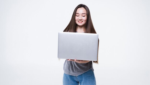 Portret uśmiechniętej kobiety azjatyckie posiadania komputera przenośnego na białym tle na szarej ścianie
