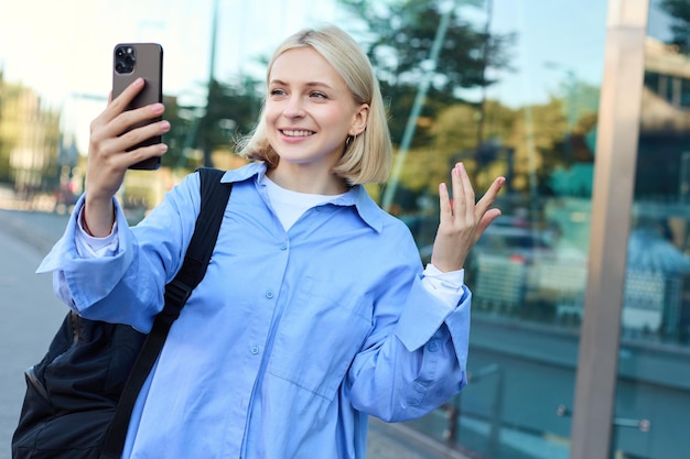 Bezpłatne zdjęcie portret uśmiechniętej kobiety, blogerki stylu życia, nagrywającej wideo na smartfonie, rozmawiającej online, patrzącej