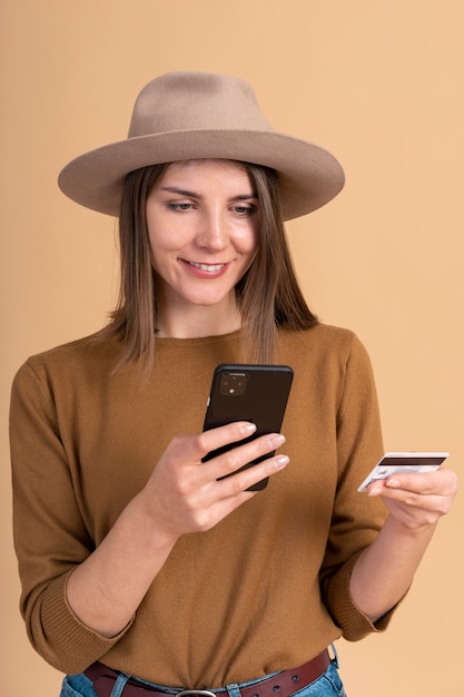 Portret uśmiechniętej kobiety w kapeluszu, rezerwującej bilety podróżne za pomocą smartfona i karty kredytowej