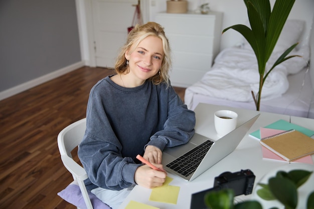Portret uśmiechniętej młodej kobiety, która uczy się na odległość za pomocą laptopa