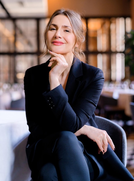 Portret uśmiechniętej, odnoszącej sukcesy bizneswoman, patrzącej w kamerę siedzącą w restauracji Biznesowa dama ze stylową fryzurą nosi elegancki garnitur Spotkanie biznesowe Atrakcyjny wygląd