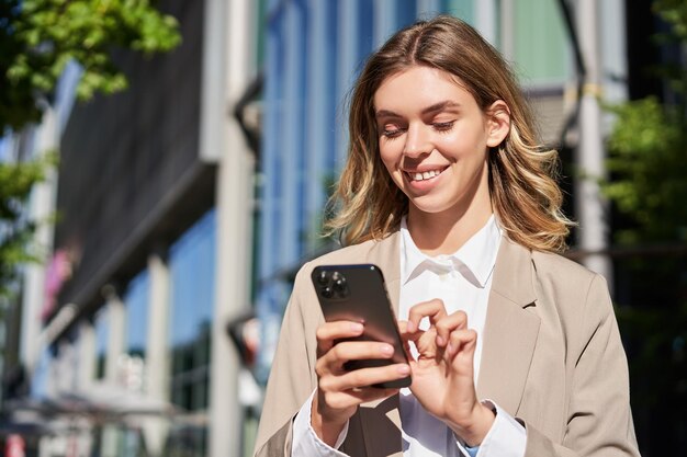 Portret uśmiechniętej pięknej bizneswoman używającej telefonu komórkowego na ulicznej korporacyjnej kobiecie stuknij ją
