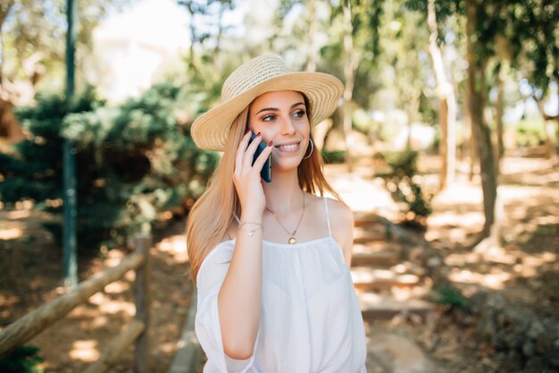 Portret uśmiechniętej pięknej kobiety rozmawiającej przez telefon w letnim parku