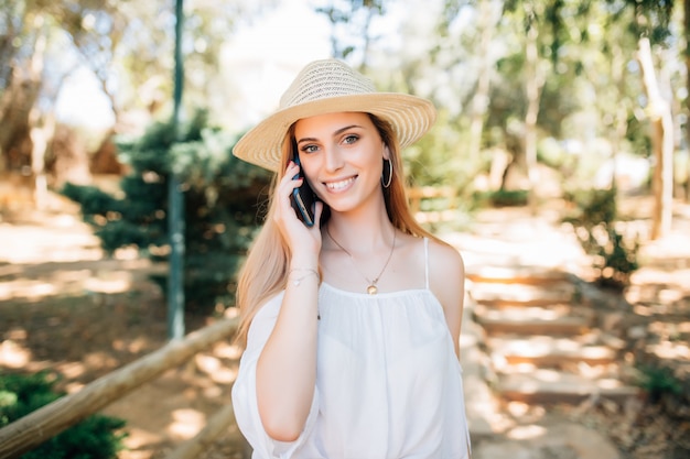Portret uśmiechniętej pięknej kobiety rozmawiającej przez telefon w letnim parku