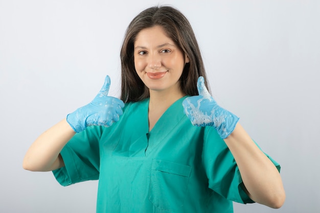 Portret Uśmiechniętej Pielęgniarki Lub Lekarza W Zielonym Mundurze Pokazując Kciuk Do Góry.