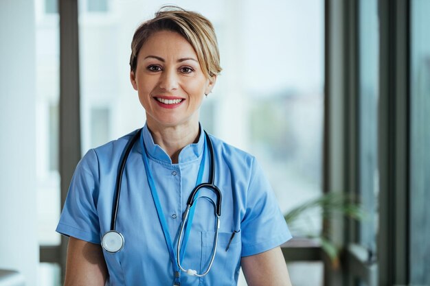 Portret uśmiechniętej pielęgniarki patrzącej na kamerę stojąc w klinice