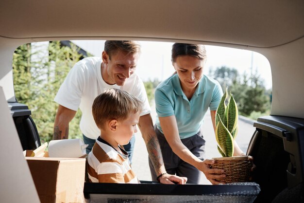 Portret uśmiechniętej rodziny ładującej pudełka w bagażniku samochodu podczas przeprowadzki do nowego domu w słońcu
