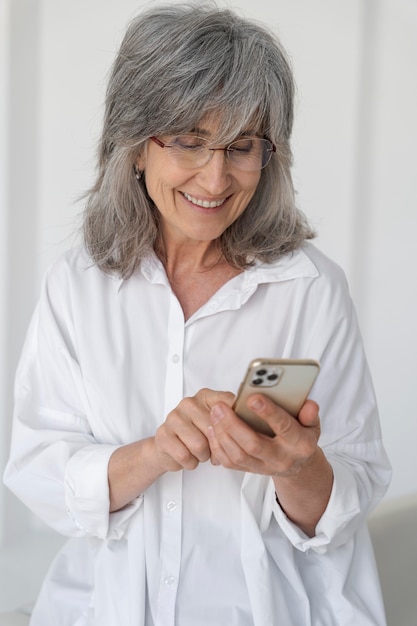 Portret uśmiechniętej starszej kobiety korzystającej z telefonu komórkowego w domu