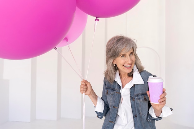 Portret uśmiechniętej starszej kobiety trzymającej filiżankę i różowe balony