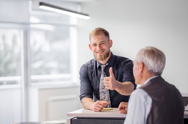 Portret uśmiechnięty biznesmen pokazuje kciuk up podpisuje wewnątrz biuro