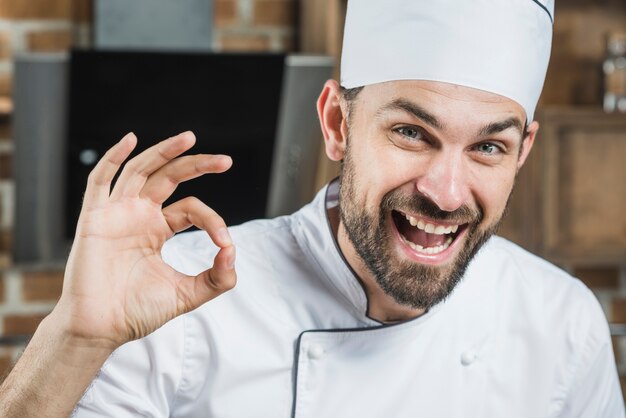 Portret uśmiechnięty męski szef kuchni pokazuje ok znaka