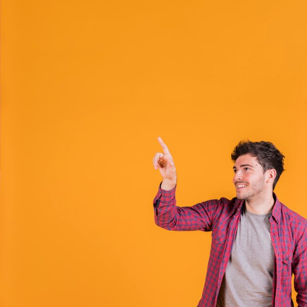 Portret uśmiechnięty młody człowiek wskazuje jego palec przeciw pomarańczowemu tłu