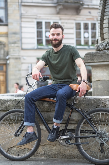Portret uśmiechnięty młody człowiek z bicyklem w mieście