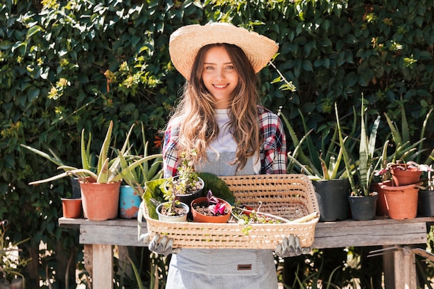 Portret uśmiechnięty młody żeński ogrodniczki mienie puszkował rośliny w koszu