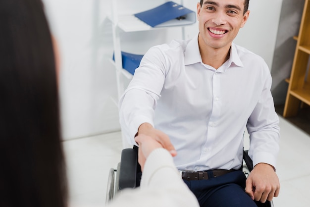Portret uśmiechnięty niepełnosprawny młody biznesmen siedzi na wózku inwalidzkim trząść rękę z bizneswomanem