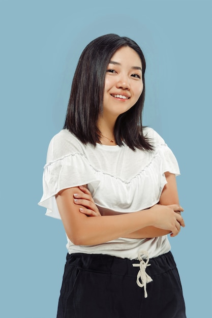 Portret w połowie długości koreański młodej kobiety na niebieskiej przestrzeni. Modelka w białej koszuli. Stojąc i uśmiechając się.
