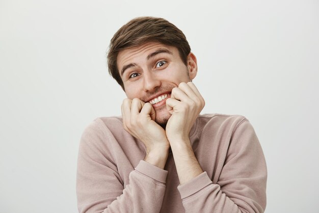 Portret zadowolonego, dobrze wyglądającego, zabawnego mężczyzny trzymającego zaciśnięte pięści w ustach