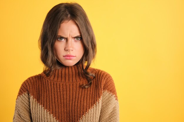 Portret zdenerwowanej dziewczyny w przytulnym swetrze ze złością patrzącą w kamerę na kolorowym tle