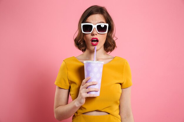 Portret zdziwiona dziewczyna trzyma filiżankę w okularach przeciwsłonecznych
