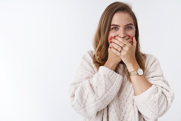 Portret zszokowanej podekscytowanej uśmiechniętej pozytywnej przystojnej europejskiej dziewczyny zaskoczonej pod wrażeniem naciskania dłoni na usta zszokowane uczenie się plotki, plotkowanie bez słowa stojące białe tło