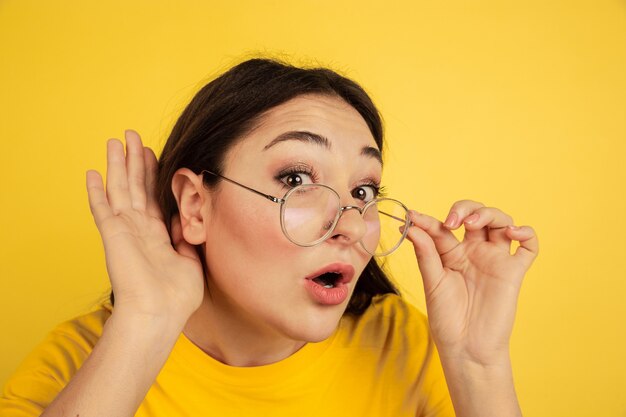 Posłuchaj tajemnic. Portret kobiety kaukaski na białym tle na żółtej ścianie. Piękna modelka brunetka w stylu casual. Pojęcie ludzkich emocji, wyraz twarzy, sprzedaż, reklama, copyspace.