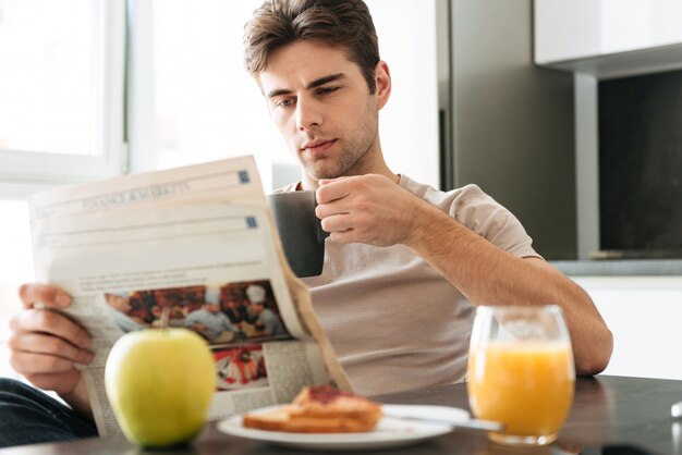 Potomstwa skoncentrowali się mężczyzna czytelniczą gazetę podczas gdy siedzący w kuchni
