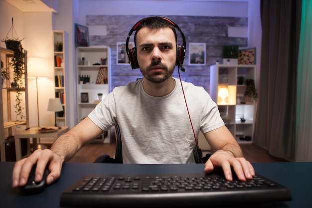Bezpłatne zdjęcie pov rywalizującego młodego mężczyzny grającego w strzelanki online na swoim komputerze w pokoju z neonowym światłem. człowiek ze słuchawkami.